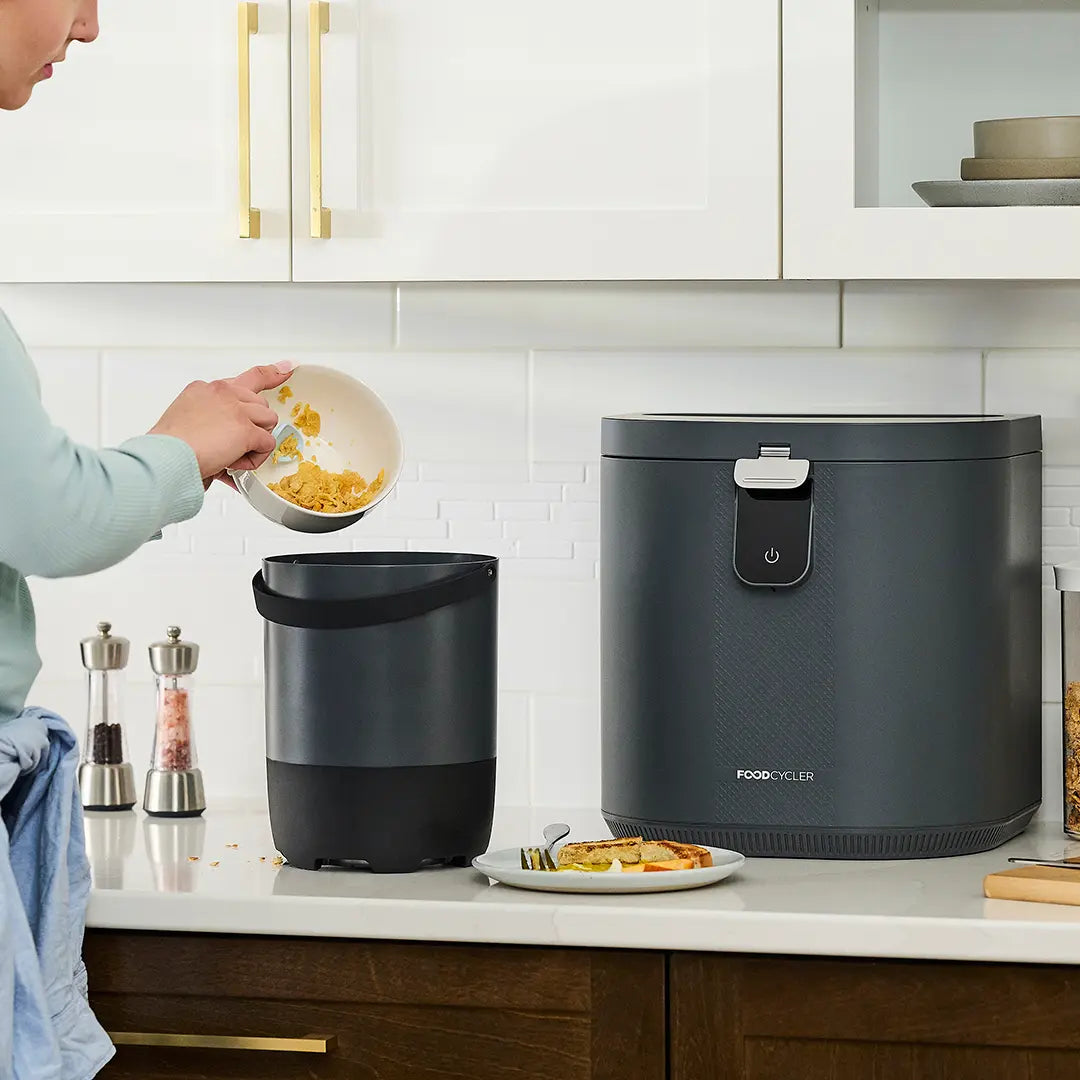 Person adding food scraps into a FoodCycler Eco 5 bucket, which sits on the kitchen counter.