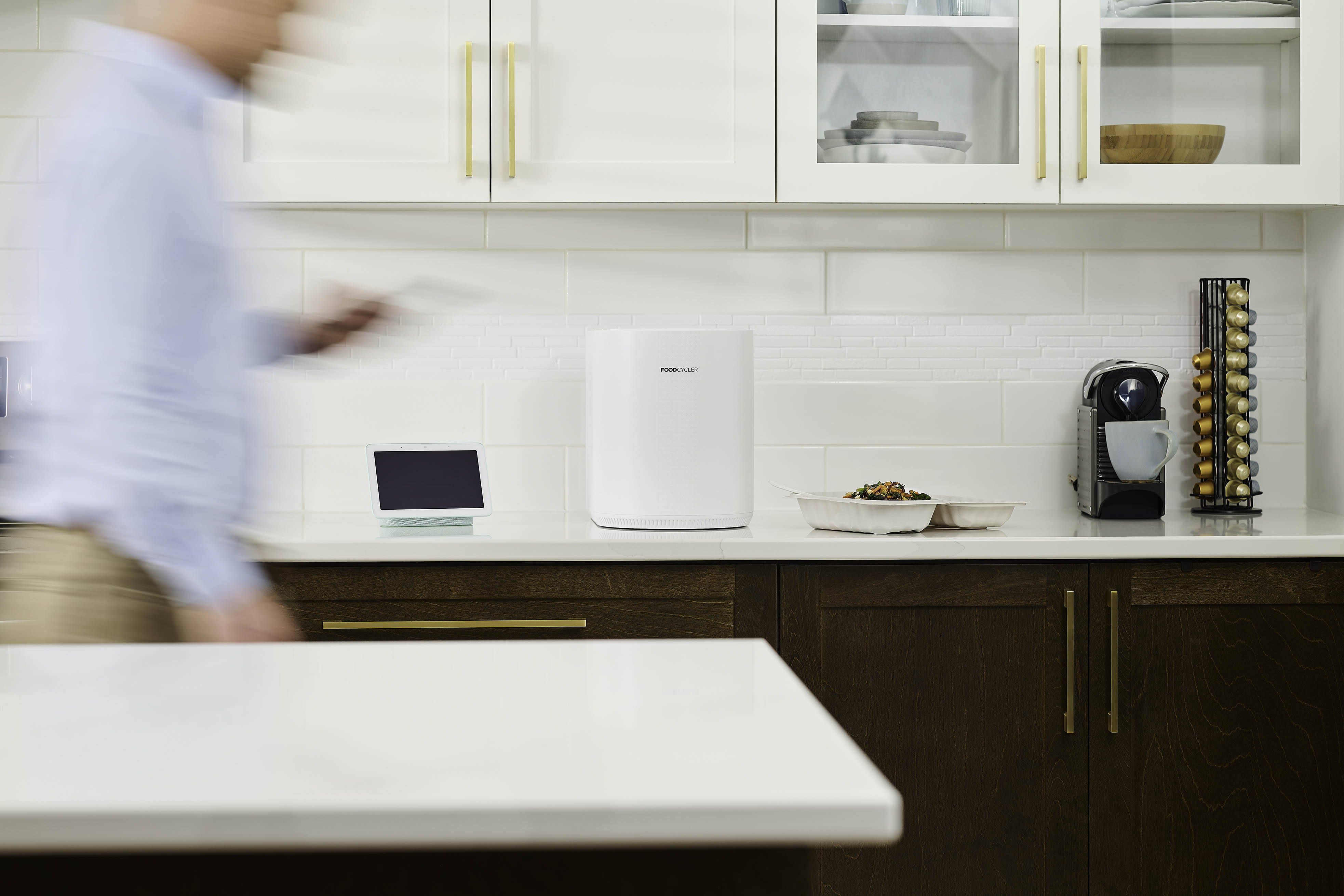 L'élégant FoodCycler Eco 3 sur le comptoir d'une cuisine, à côté d'un appareil domestique intelligent, de restes prêts à être ajoutés au FoodCycler et d'une machine à expresso. Il s'adapte à votre style de vie.