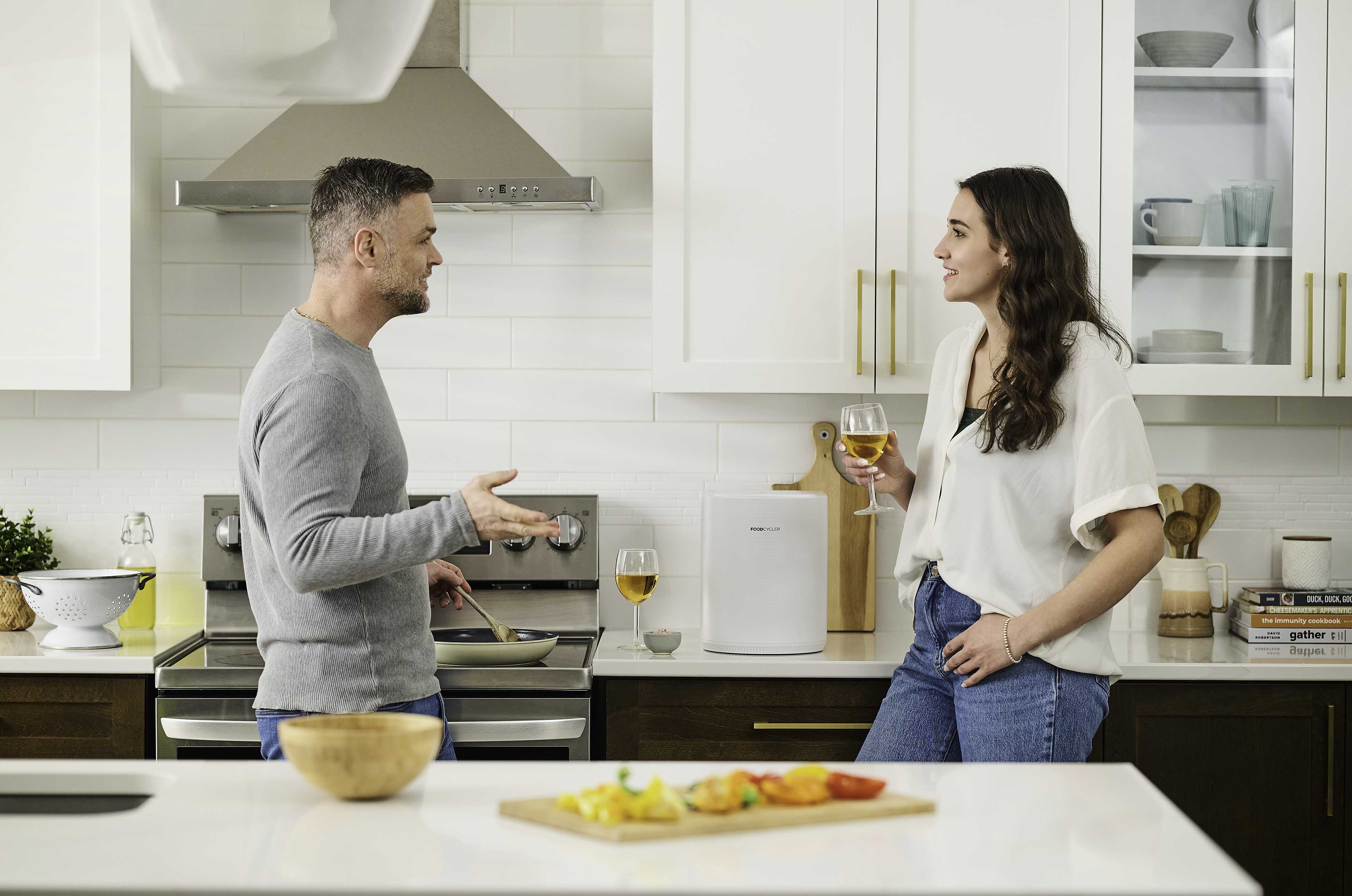 Couple enjoying a glass of wine while cooking dinner; the sleek and compact FoodCycler Eco 3 sits on their countertop
