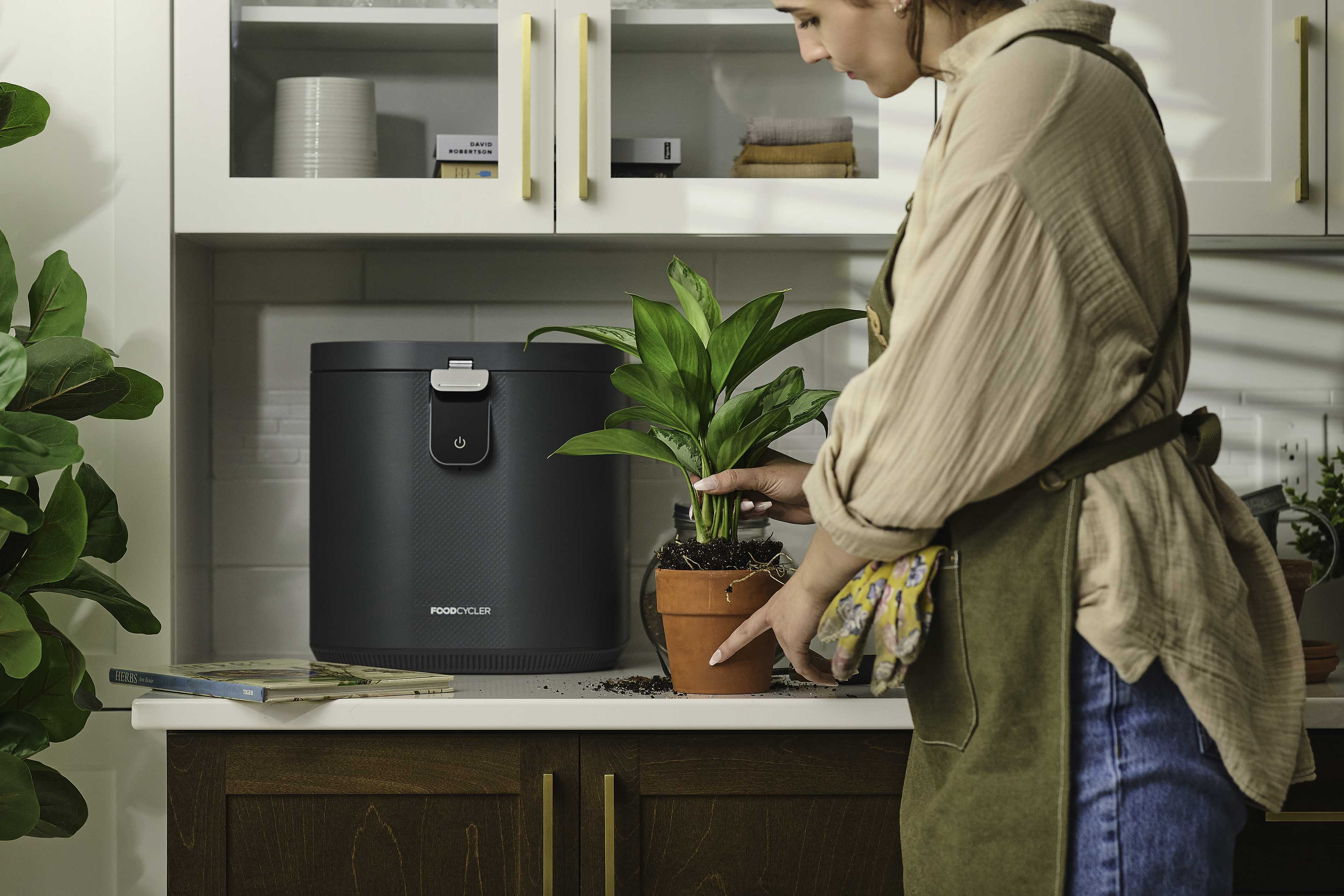 Person putting a plant on the counter; FoodCycler Eco 5 behind it.