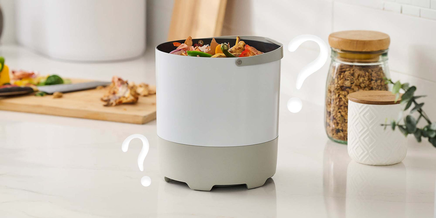 A white removable FoodCycler food waste bucket filled with kitchen scraps sitting on a white countertop, flanked by floating question mark graphics.