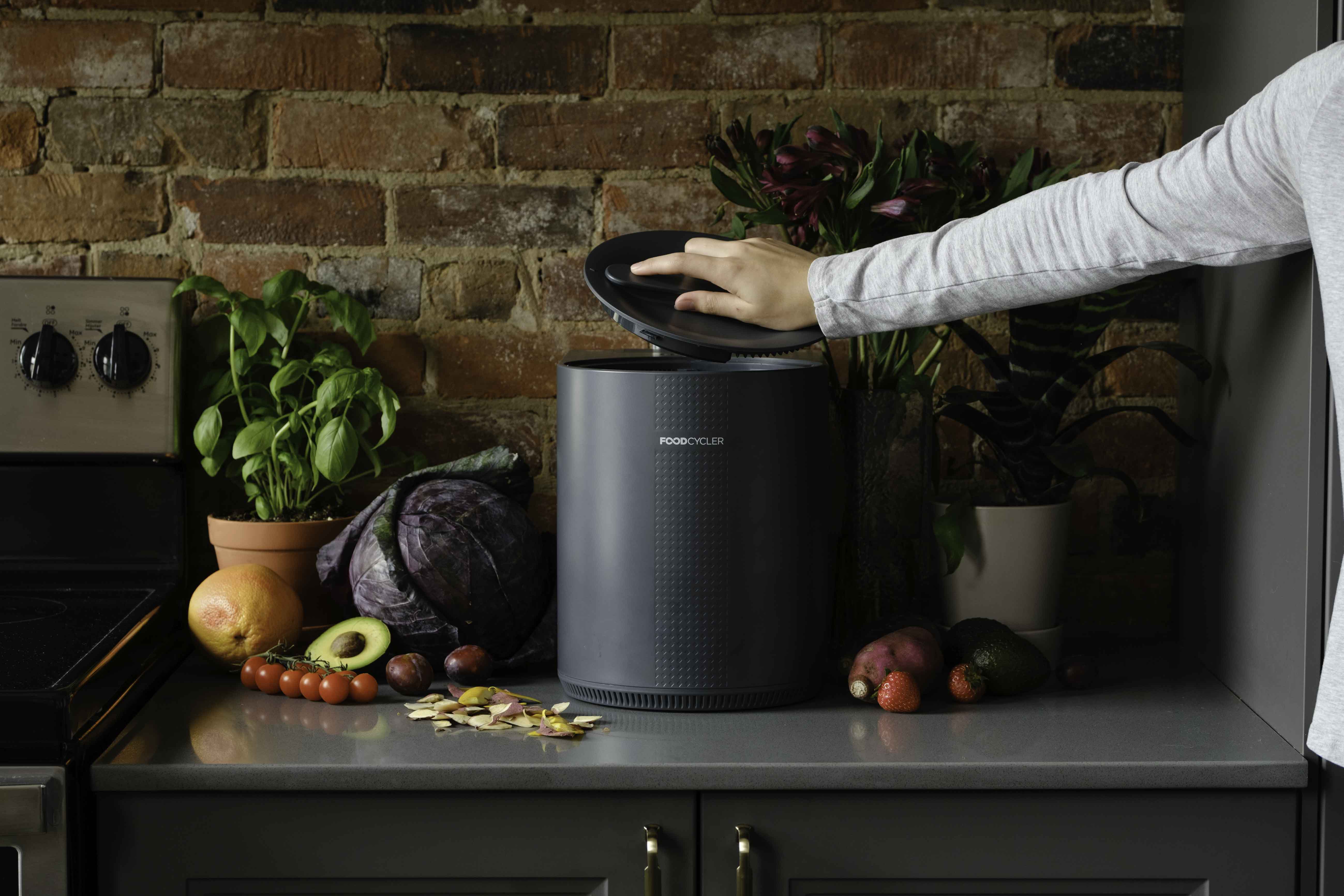 Grey FoodCycler Eco 3 on a kitchen counter with a person putting the lid on